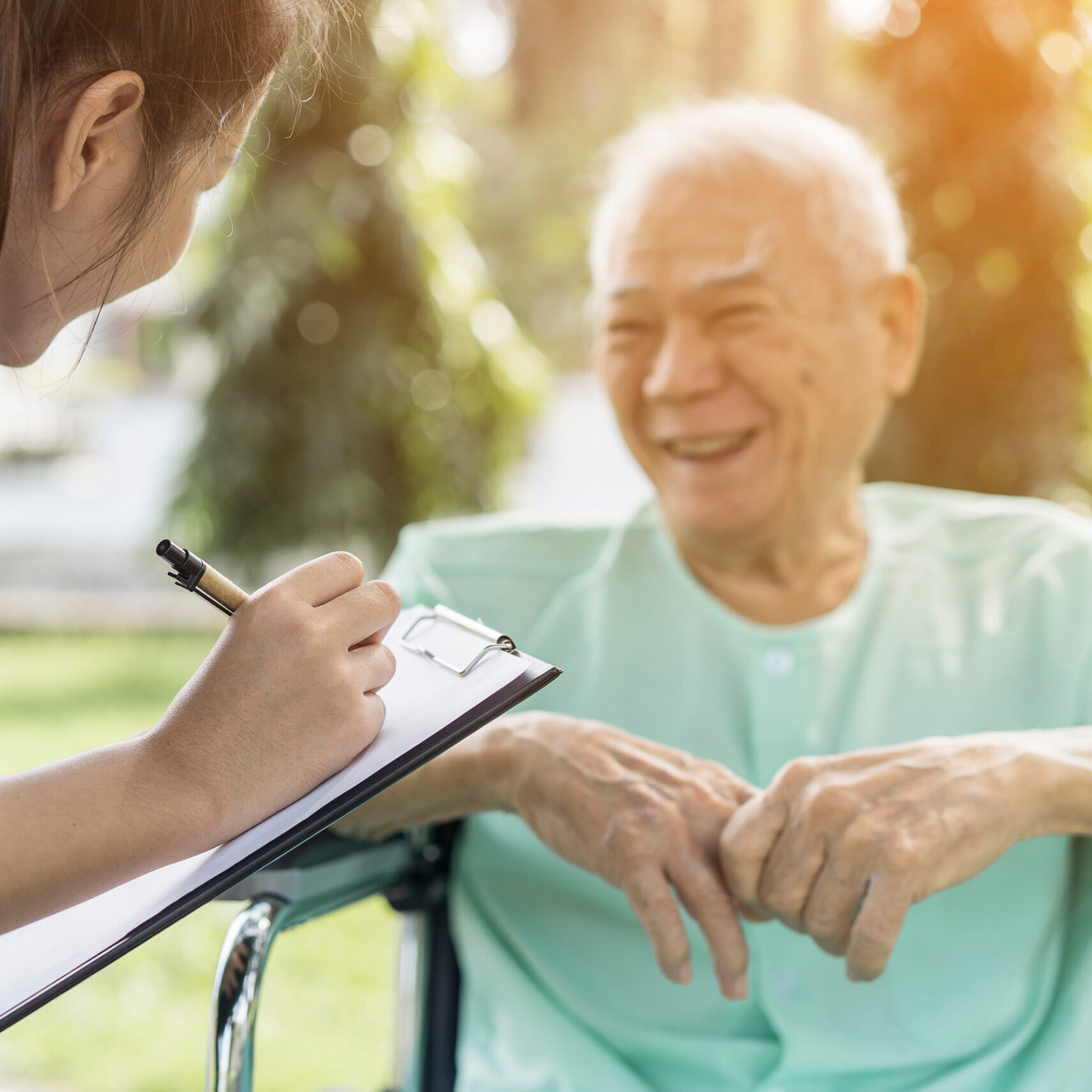 Female care worker serving checklist health to Happy smiling Asian senior man in a wheelchair relaxing while outside on park at Good environment and fresh air.Assistant,Retirement or elderly caregiver