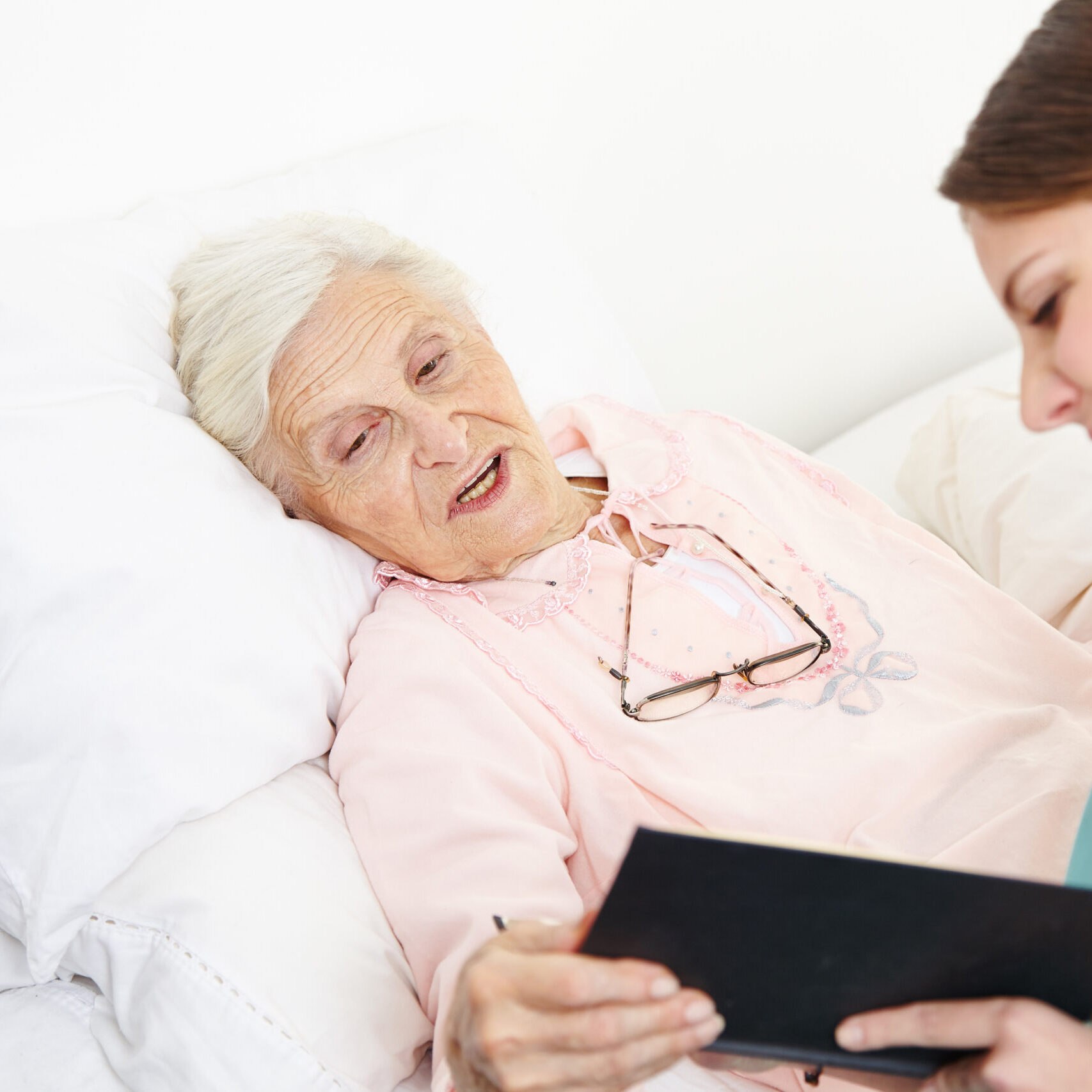 Geriatric nurse reading book to senior citizen woman in bed